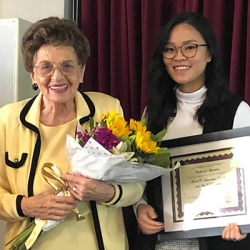 A older woman holding flowers with a younger woman holding a framed certificate